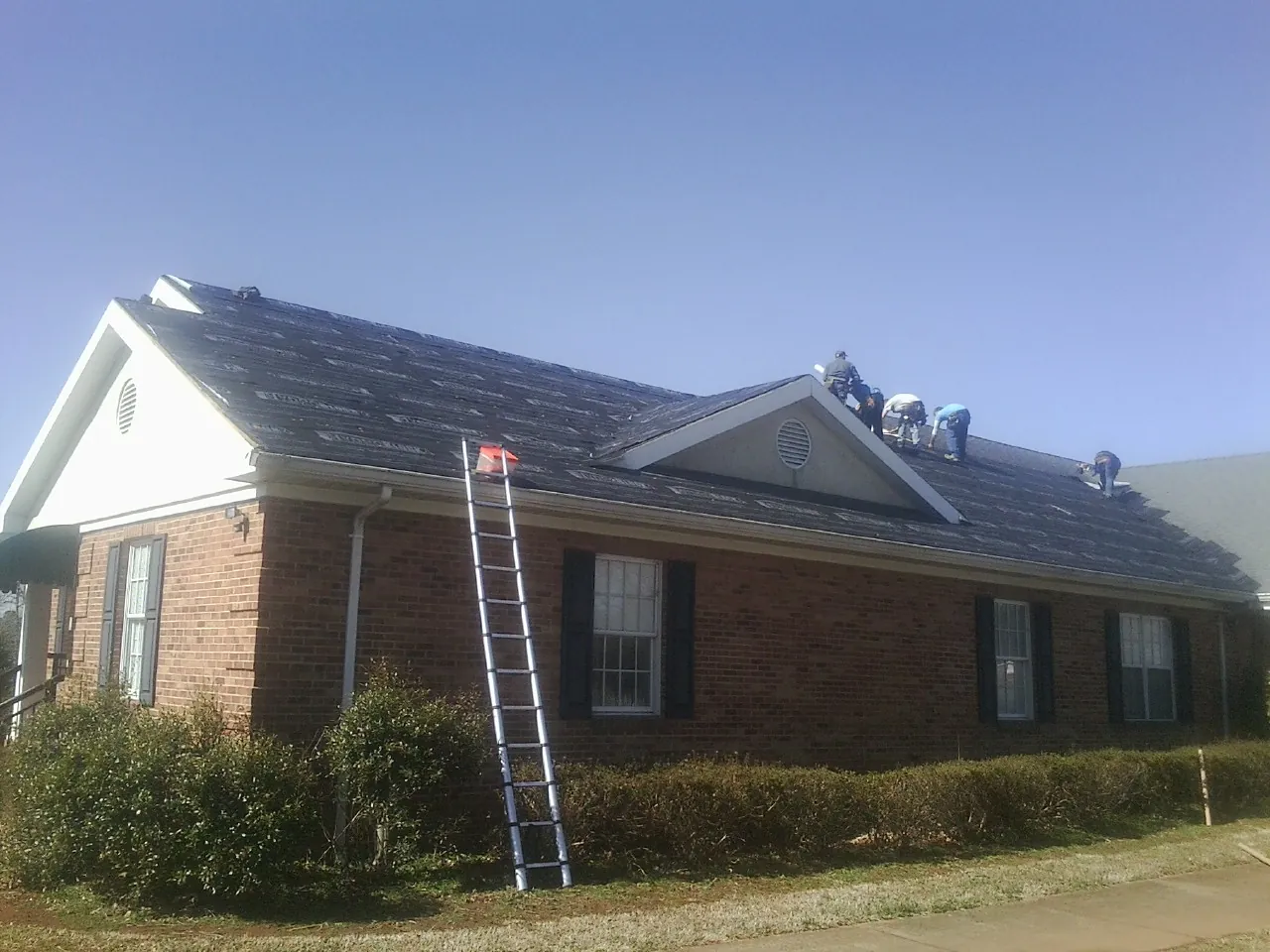 Crew tearing shingles off a brick ranch roof with a ladder set — Emergency Roof Repair work by our crew in Foxboro