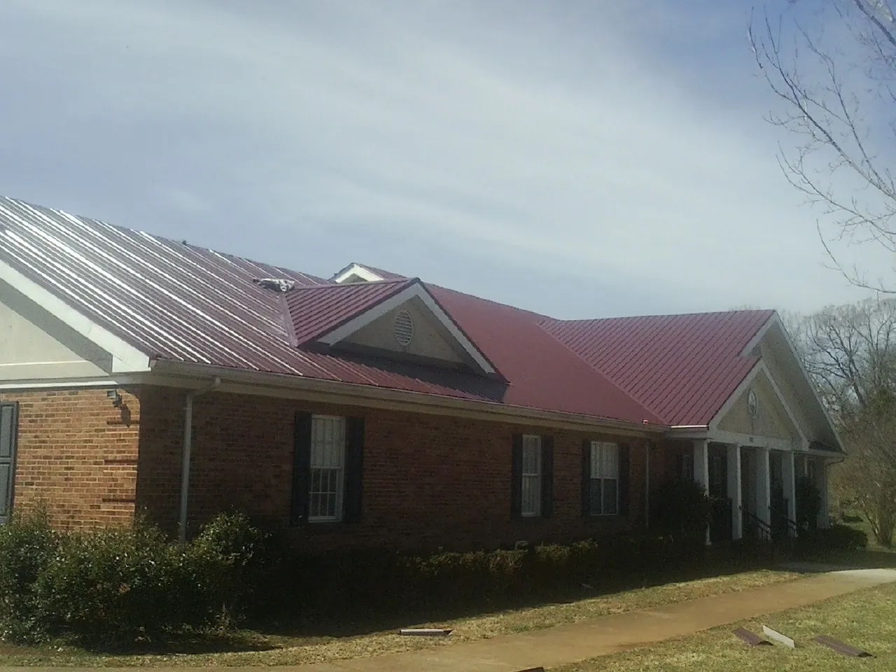 Red metal roof with gabled entries on a long brick building, from a Hail Damage Roof Repair job in Foxboro