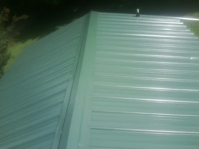 New green metal panels meeting at the ridge of a roof — Flat Roof Repair work by our crew in Foxboro