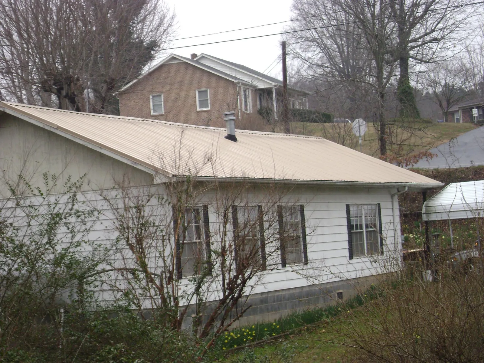 Tan metal roof on a white sided house set into a hillside — Commercial Roofing by Roofing Brothers in Foxboro